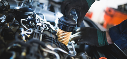 En hånd som trekker ut motoroljefilteret fra motoren