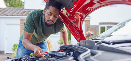 En person som reparerer bilen sin med panseret oppe